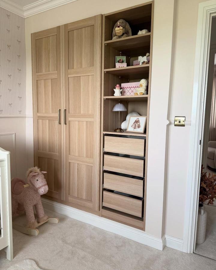 Warm oak IKEA PAX nursery ideas wardrobe from @homebyrosie. Built-in storage with blush wallpaper and open shelves.