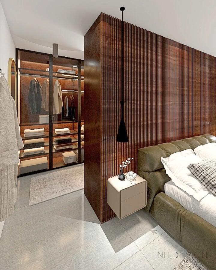 Warm walnut wood bedroom divider from @nhdotdesign. Slatted screen conceals a glass-front wardrobe beside an olive sofa.