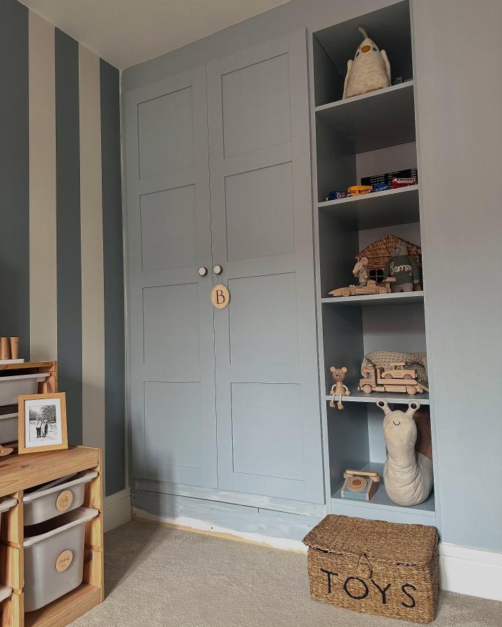 Blue-gray built-in bedroom storage from @ourownhygge. Paneled PAX wardrobe with open toy shelves and woven basket.