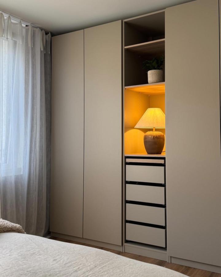 Warm beige PAX wardrobe from @ourwabisabihome. Soft lighting and open shelving beside a small bedroom.