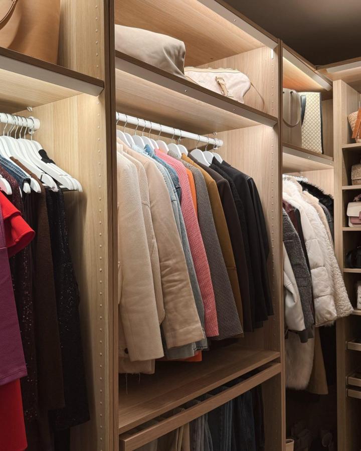 Warm woodgrain walk-in closet from @simonavantruba. White rails, open shelves, and neatly arranged neutral clothing.