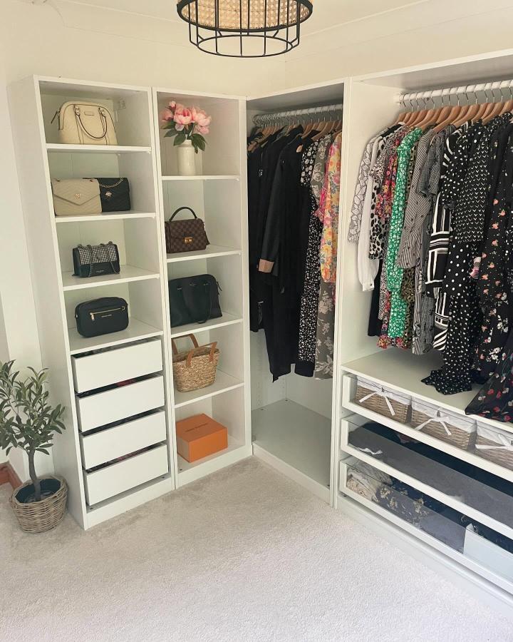 White open-shelf walk-in closet from @atthemeadows. Floral dresses, handbags, drawers, and woven baskets create a polished wardrobe.