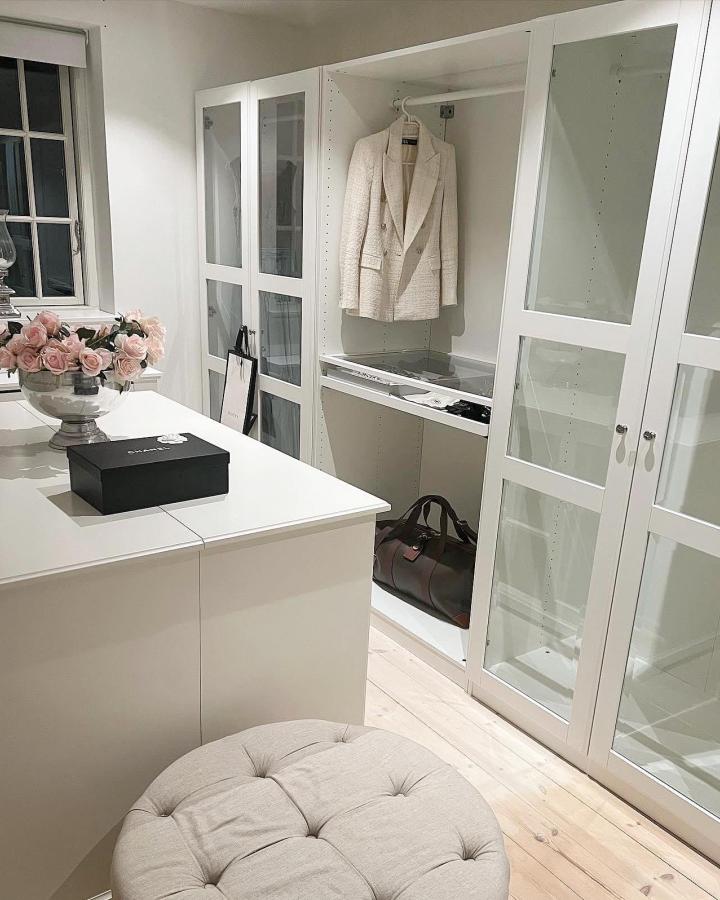 White glazed-door walk-in closet from @ingridivarson. Cream jacket, island, beige ottoman, and pink roses soften the bright PAX storage.