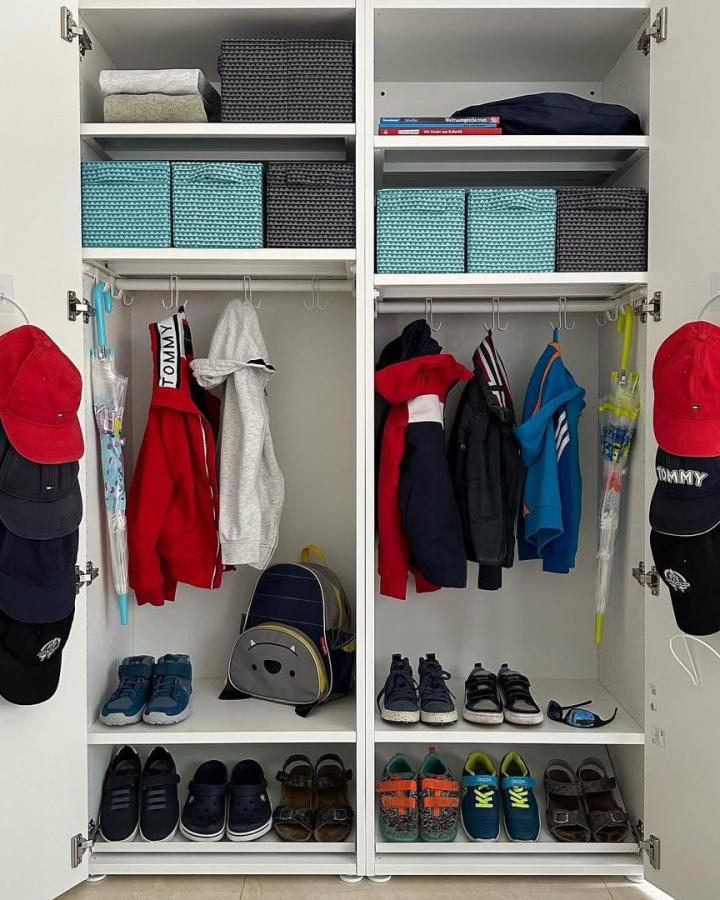 White organized kids' wardrobe from @lumei.kids.interior.organizing. Woven turquoise baskets, hooks, shoes, and colorful jackets create tidy storage.
