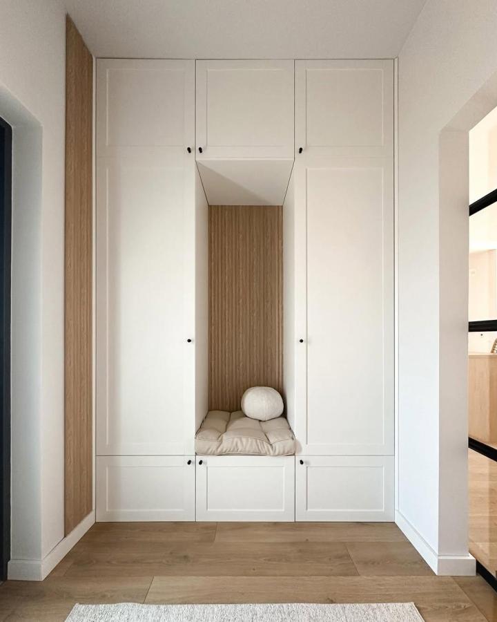 White framed built-in wardrobe from @mamamikolaja_. Warm wood reading nook with cushioned bench.