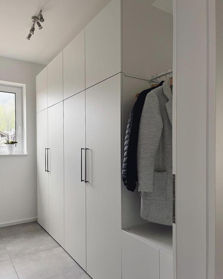 White hallway PLATSA wardrobe from @debbies.zuhause. Open coat rail, black handles, and smooth tall cabinets.