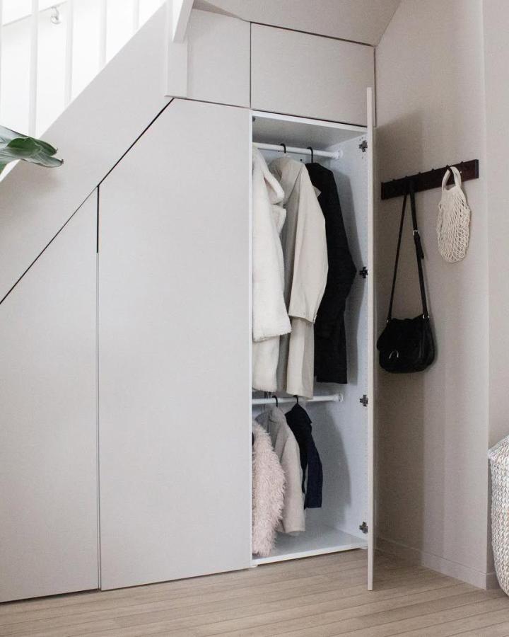 White under-stair wardrobe from @nordicbyj. Open doors reveal organized hanging storage beside a dark wood rail.