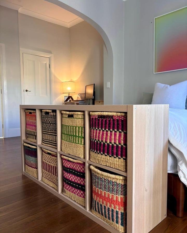 Warm oak Low KALLAX room divider from @africancreationsbaskets. Woven multicolor baskets separate a bedroom from a workspace.