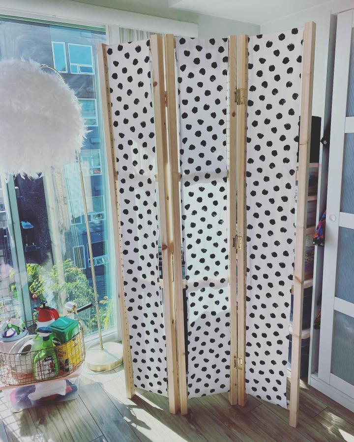 White and black spotted folding divider from @pinkmimosabyjacinta. Natural wood frames separate a bright small room.