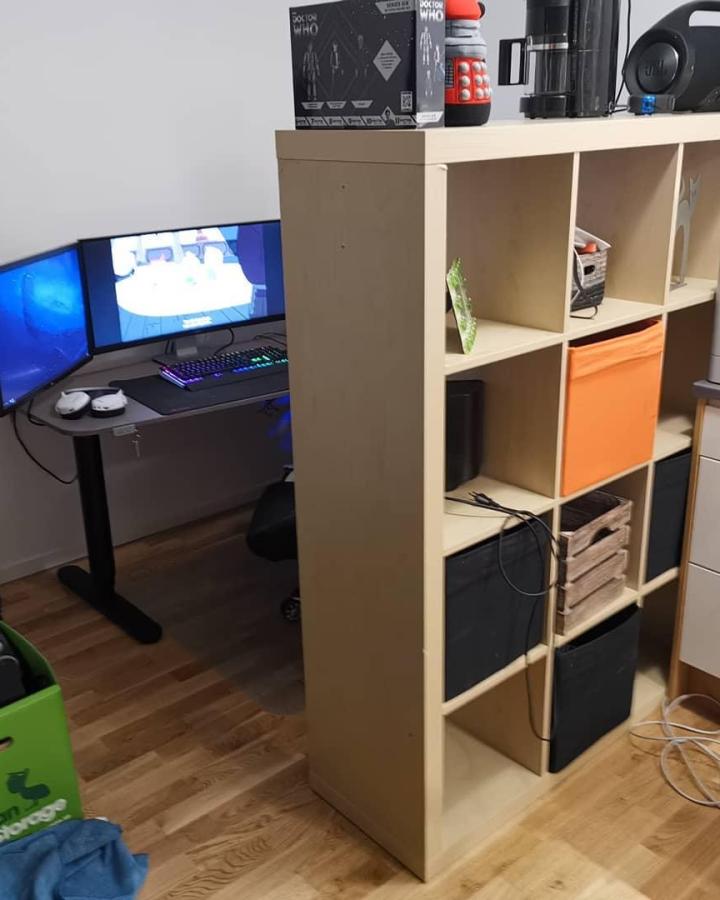 Pale wood KALLAX gaming room divider from @henkon. Open cubes separate a compact workspace from the living area.