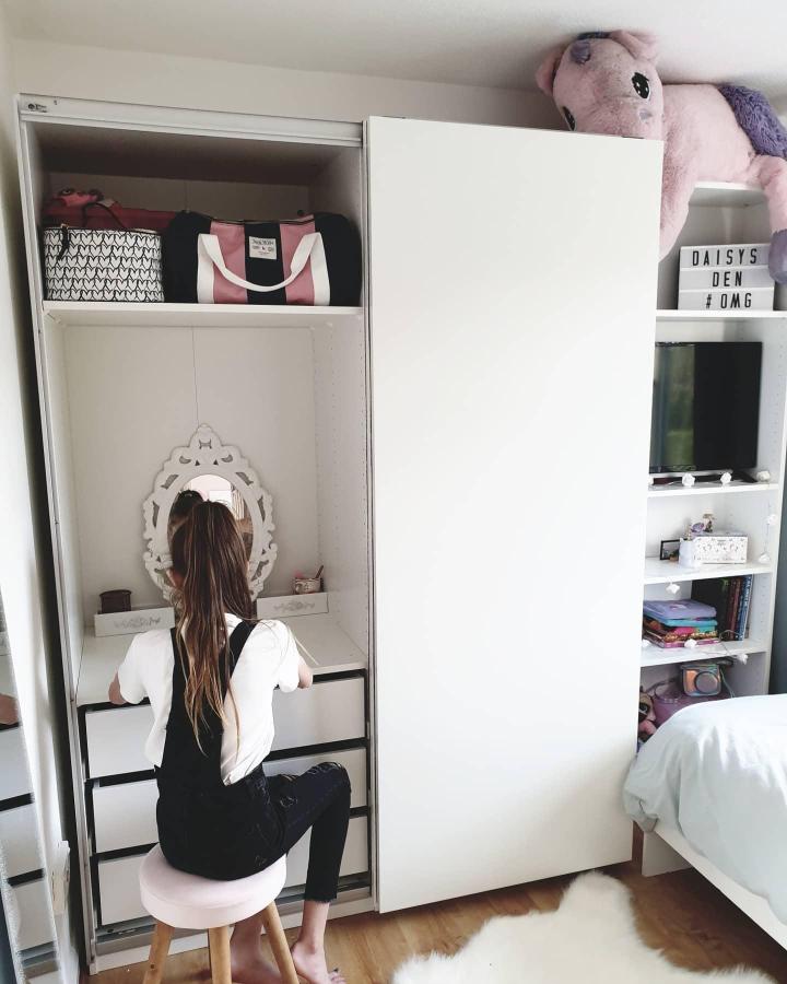 White IKEA PAX bedroom nook from @makeourhousebigger. Built-in vanity, mirror, drawers, shelving, and pink plush toy.