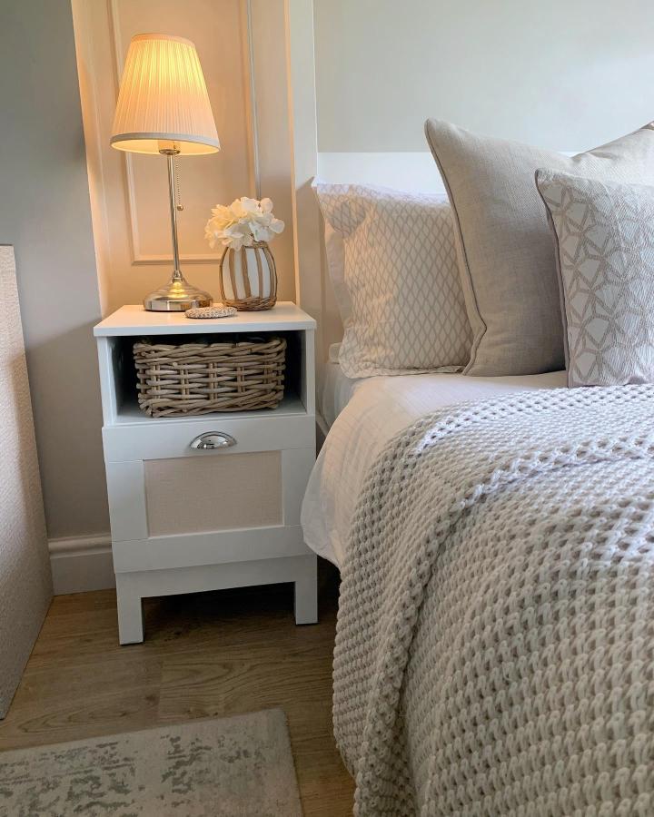 White IKEA BRIMNES bedside table from @dreah.home. Wicker basket adds storage beside a cozy layered bed.