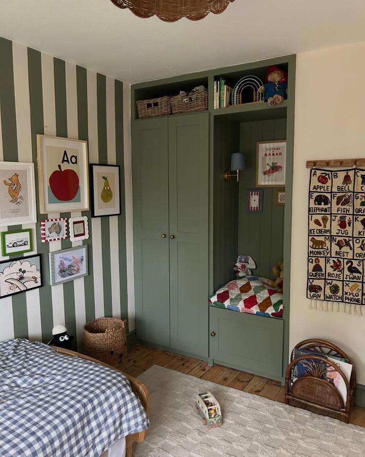 Olive green IKEA PAX bedroom storage from @inthedoghouse___. Built-in nook, striped walls, wicker baskets, and colorful quilt maximize a compact room.