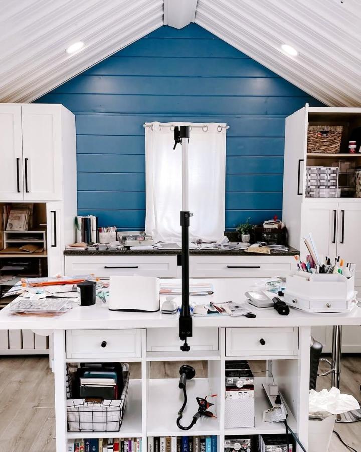 Teal shiplap IKEA craft room from @ashleyandersoncreates. White cabinets frame an organized island workspace.