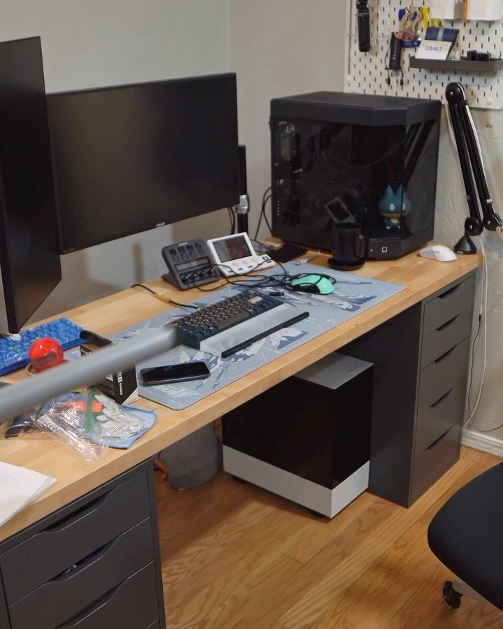 IKEA ALEX desk setup with a warm wood desktop, dual monitors, and organized gaming accessories