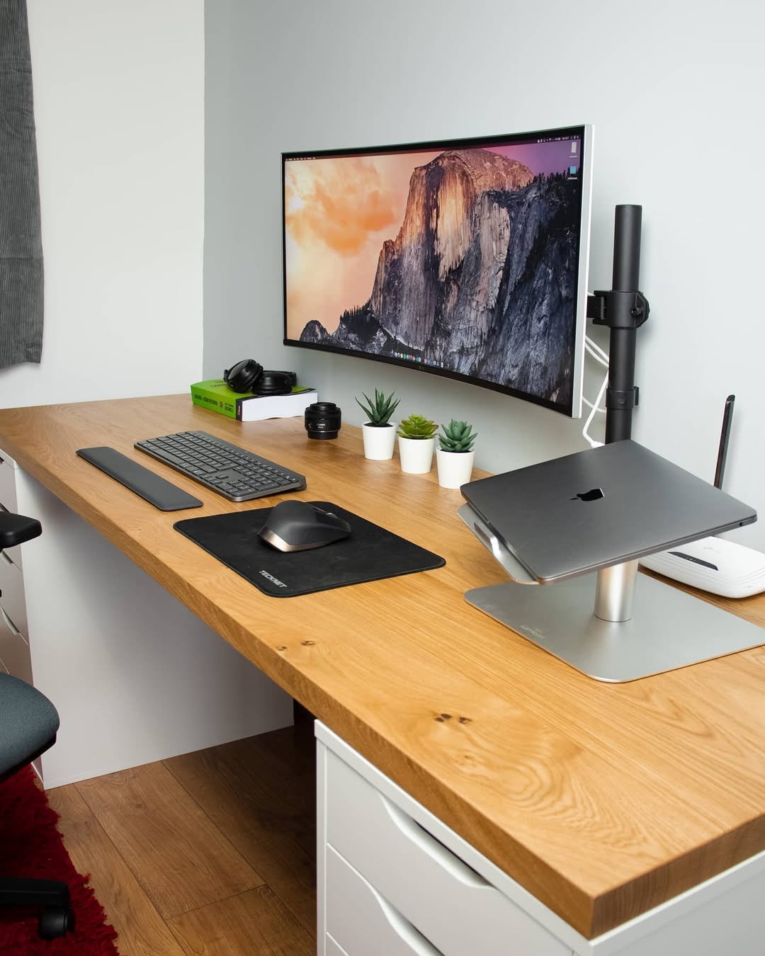 Warm oak desktop with white ALEX drawer units, ultrawide monitor, laptop stand, and organized accessories