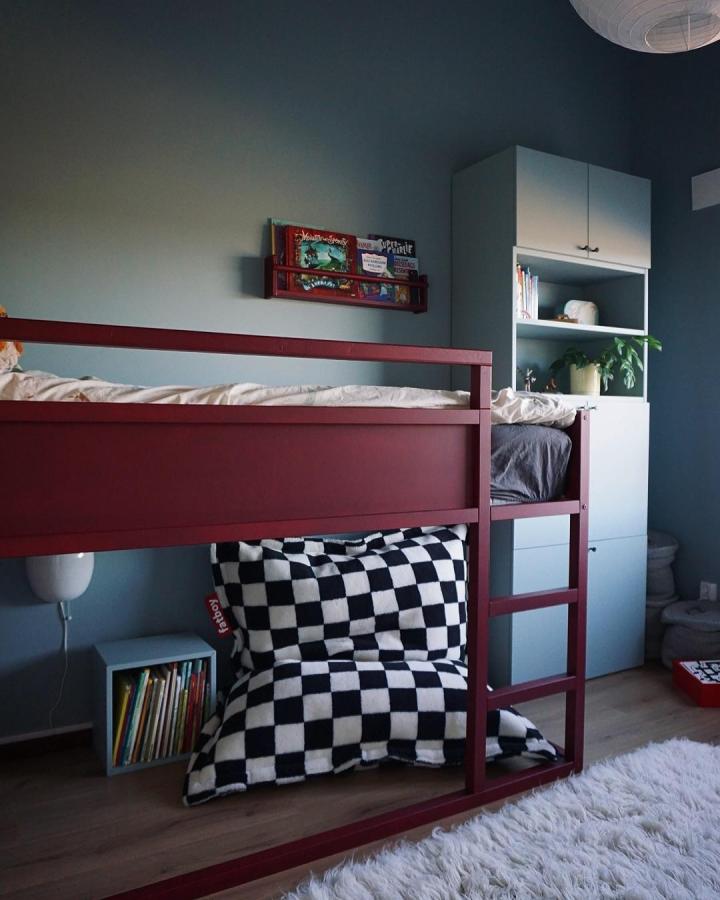 Burgundy-painted wooden KURA bunk bed from @ragnegardlinne. Checkerboard blanket and book storage suit a boyโs bedroom.