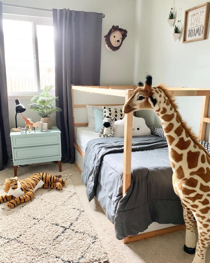 Natural wood giraffe-themed KURA bed from @cali_home_design. Gray bedding, plush safari toys, and soft green dresser suit boysโ rooms.