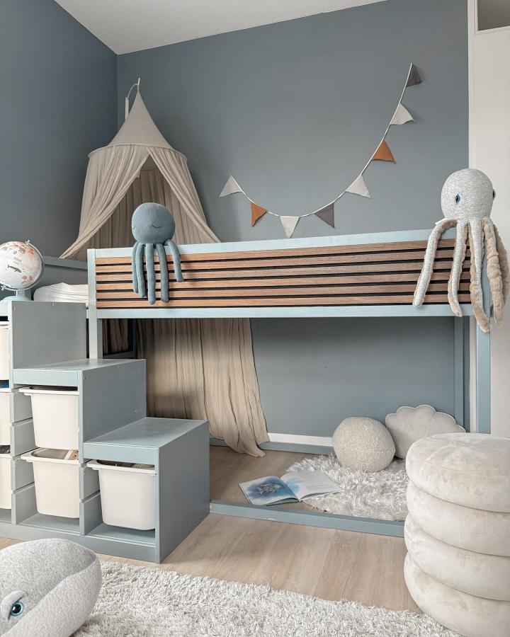Pale blue-gray KURA loft bed from @interieurbijrebecca. Natural wood slats, canopy nook, bunting, and plush octopus accents.