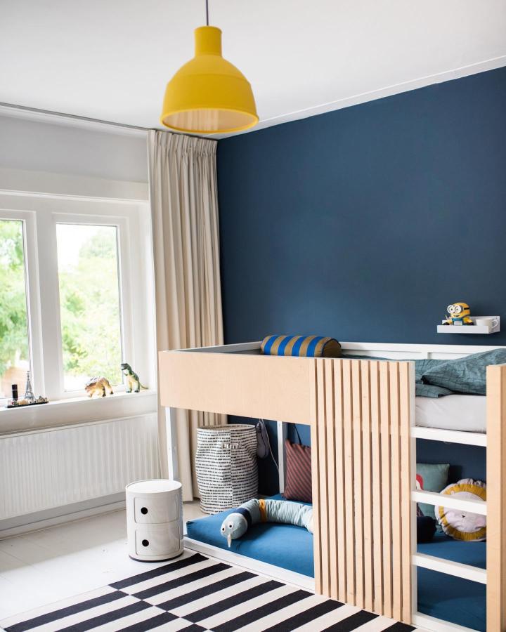 Pale wood slatted KURA bed from @keekshuis. Navy boysโ bedroom with blue bedding and yellow pendant.