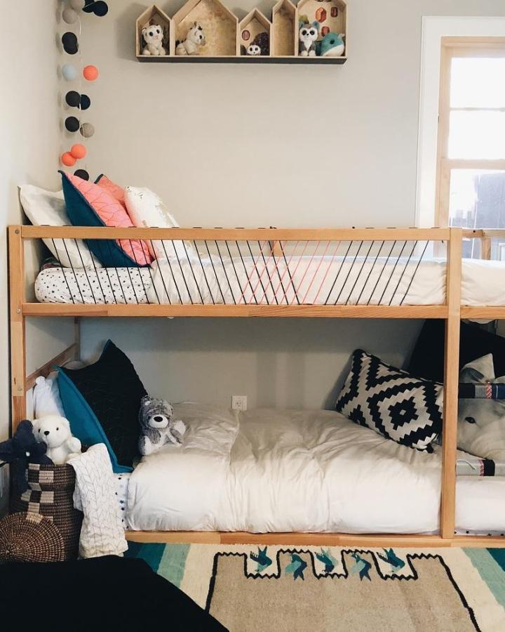 Warm wood shared-room Kura bunk from @relativerenovations. White bedding, rope rails, colorful pillows, and toy shelves.