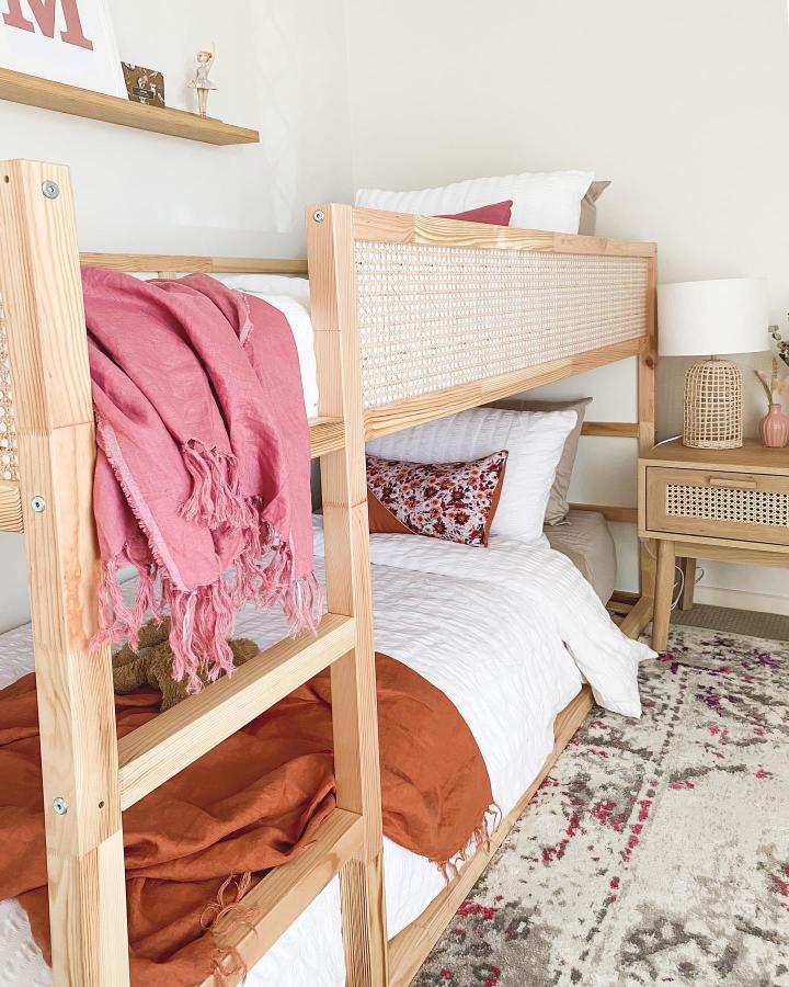 Natural pine cane-panel bunk bed from @thesomewheretribe. Pink and terracotta bedding create a warm shared childrenโs room.