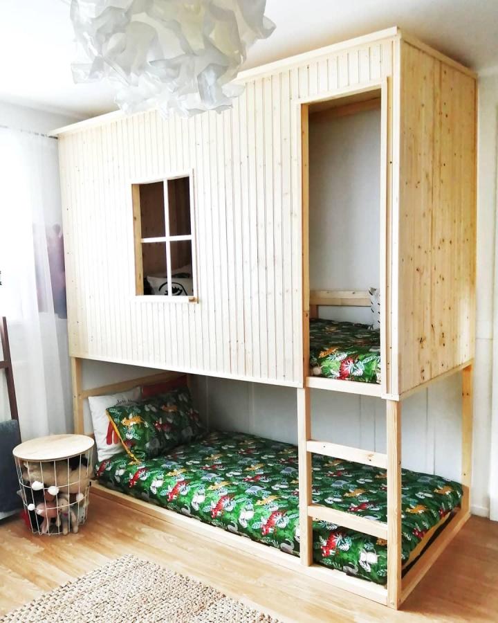 Pale slatted wood shared bedroom bunk from @mmebanasik. House-shaped IKEA KURA nook with green botanical bedding.